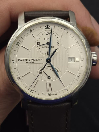 Baume & Mercier GMT automatic dual time power reserve watch with black dial and stainless steel case.