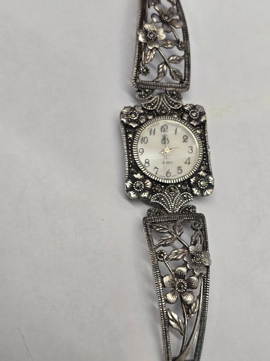 Vintage floral bracelet watch by Reeves and Sons with marcasite accents, ornate silver design, and quartz movement.