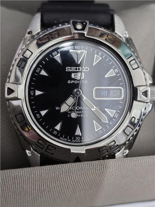Seiko 5 Sports automatic watch with box and papers, showing the watch face with black dial and stainless steel bracelet.