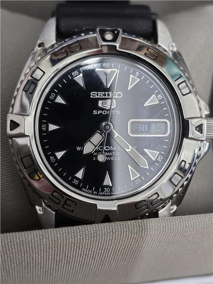 Seiko 5 Sports automatic watch with box and papers, showing the watch face with black dial and stainless steel bracelet.