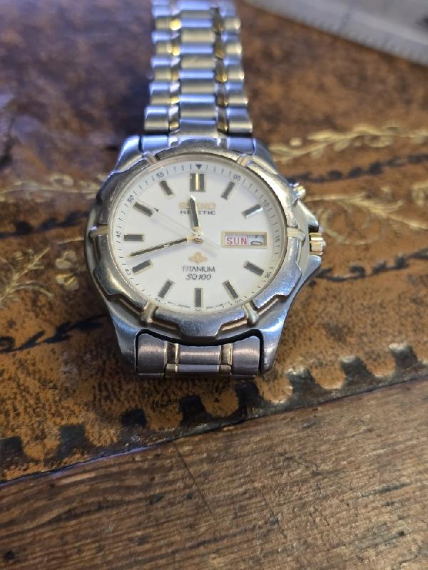 Seiko kinetic titanium SQ100 watch with black dial and silver band, showcasing a sleek modern design.