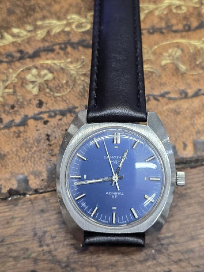 Vintage Longines 1972 Munich Olympics watch with gold-tone case and black leather strap, showcasing Olympic logo and time display.