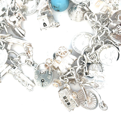 Silver charm bracelet with intricate designs, weighing 128.8g, featuring multiple charms and a secure clasp.