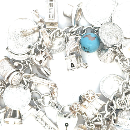 Silver charm bracelet weighing 128.8g with various decorative charms, unbranded jewelry piece on a neutral background.