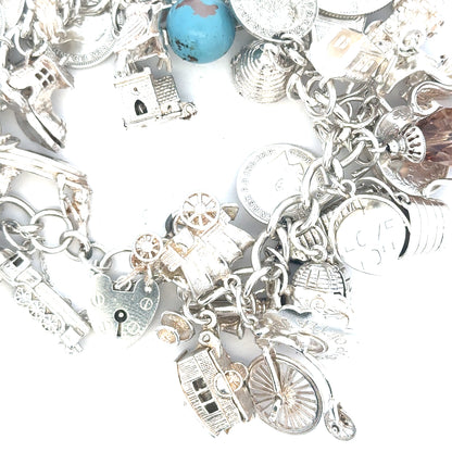 Silver charm bracelet weighing 128.8g with intricate designs, featuring various charms and a secure clasp.