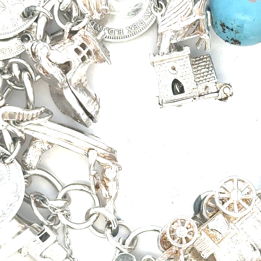 Silver charm bracelet with intricate designs, weighing 128.8g, featuring multiple charms on a linked chain.