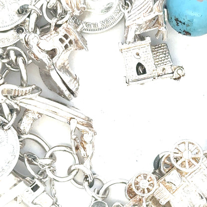 Silver charm bracelet with intricate designs, weighing 128.8g, featuring multiple charms on a linked chain.