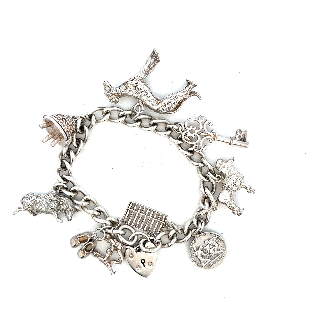 Silver charm bracelet with multiple charms, unbranded, weighs 60.1 grams, displayed on a neutral background.