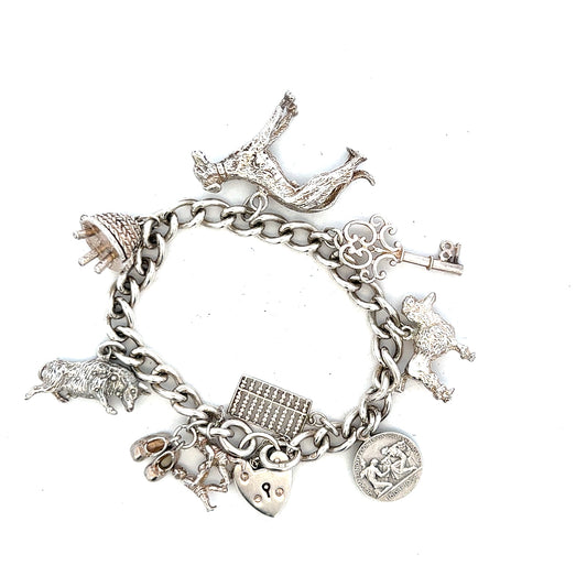 Silver charm bracelet with multiple charms, unbranded, weighs 60.1 grams, displayed on a neutral background.