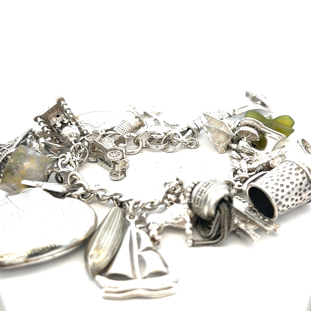 Silver charm bracelet with intricate designs, weighs 83.4g, featuring multiple charms on a sturdy silver chain.