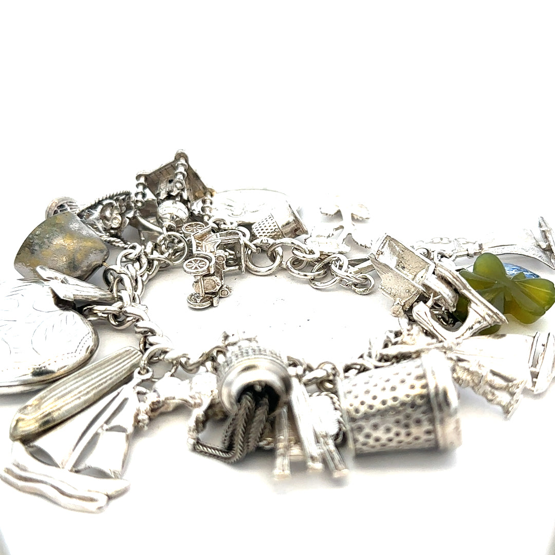Silver charm bracelet weighing 83.4g with various charms, featuring detailed metalwork and a secure clasp.