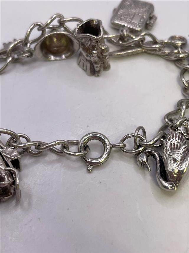 Silver charm bracelet with intricate designs, weighs 33.9g, featuring multiple charms on a durable silver chain.